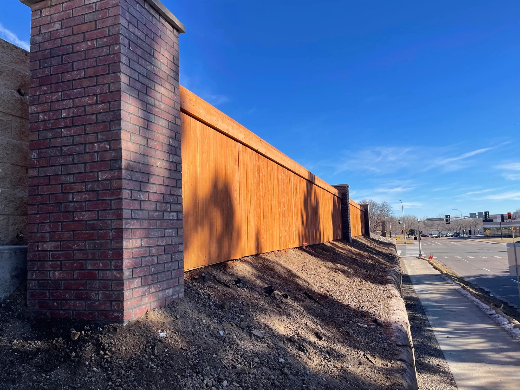Brick column and cedar privacy fence installed at Heritage Shopping Center under a deep blue sky